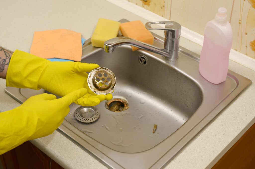 Cleaner in rubber gloves shows waste in the plughole protector of a kitchen sink