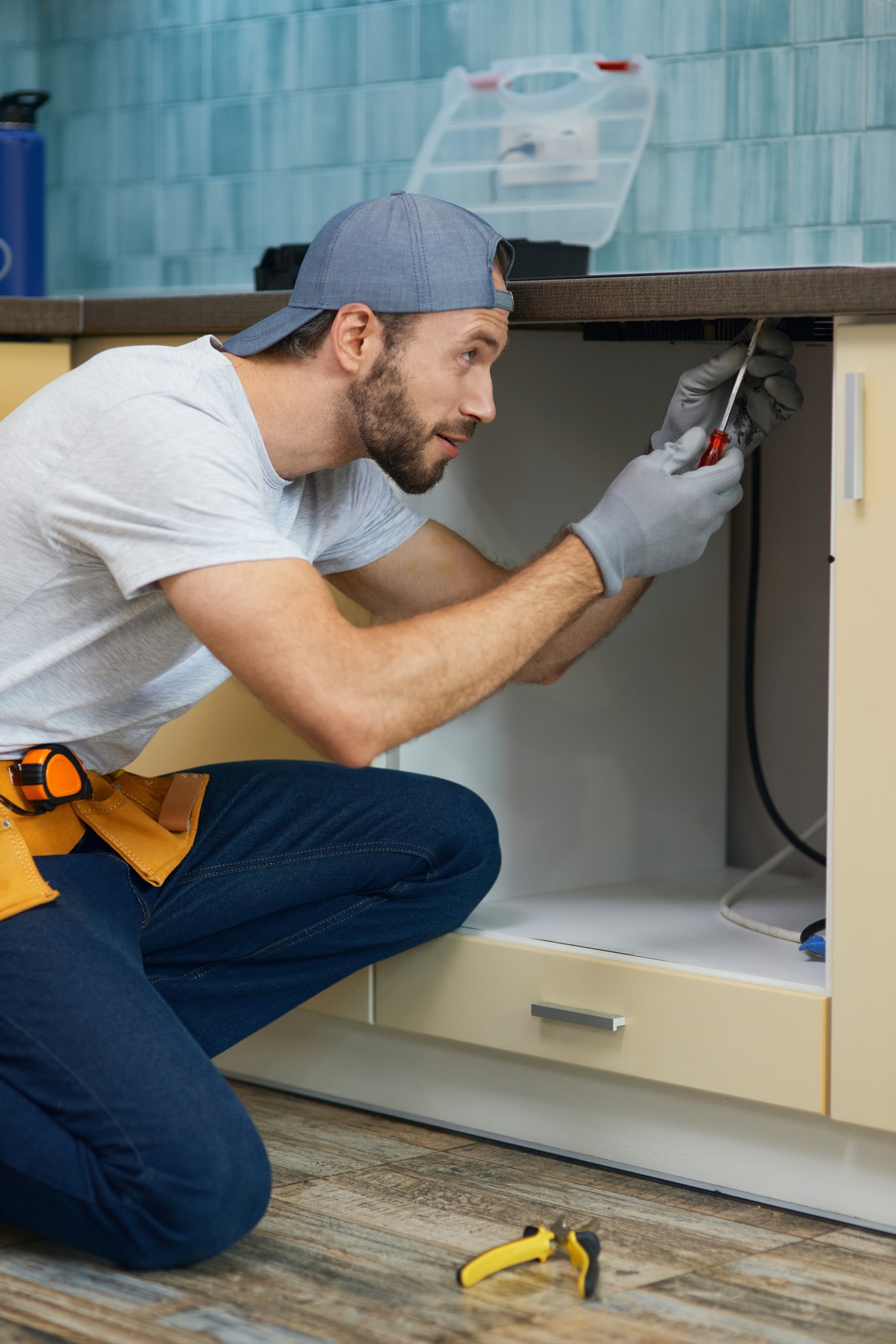 Fixing leaks. Focused young repairman, professional plumber wearing tool belt crouching on the